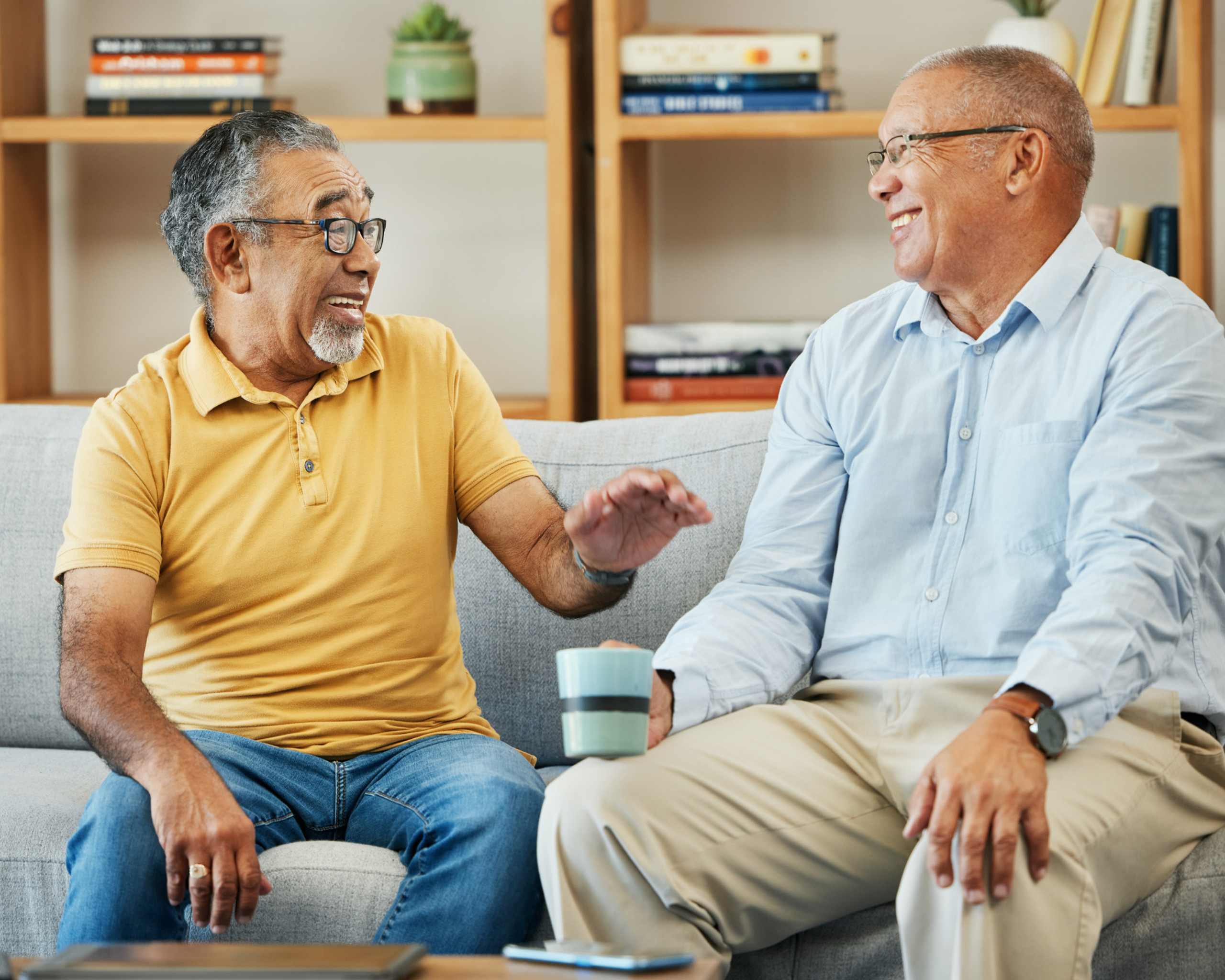Two friends share a lighthearted moment, reminiscing about old times over coffee in a cozy living room filled with warmth and laughter