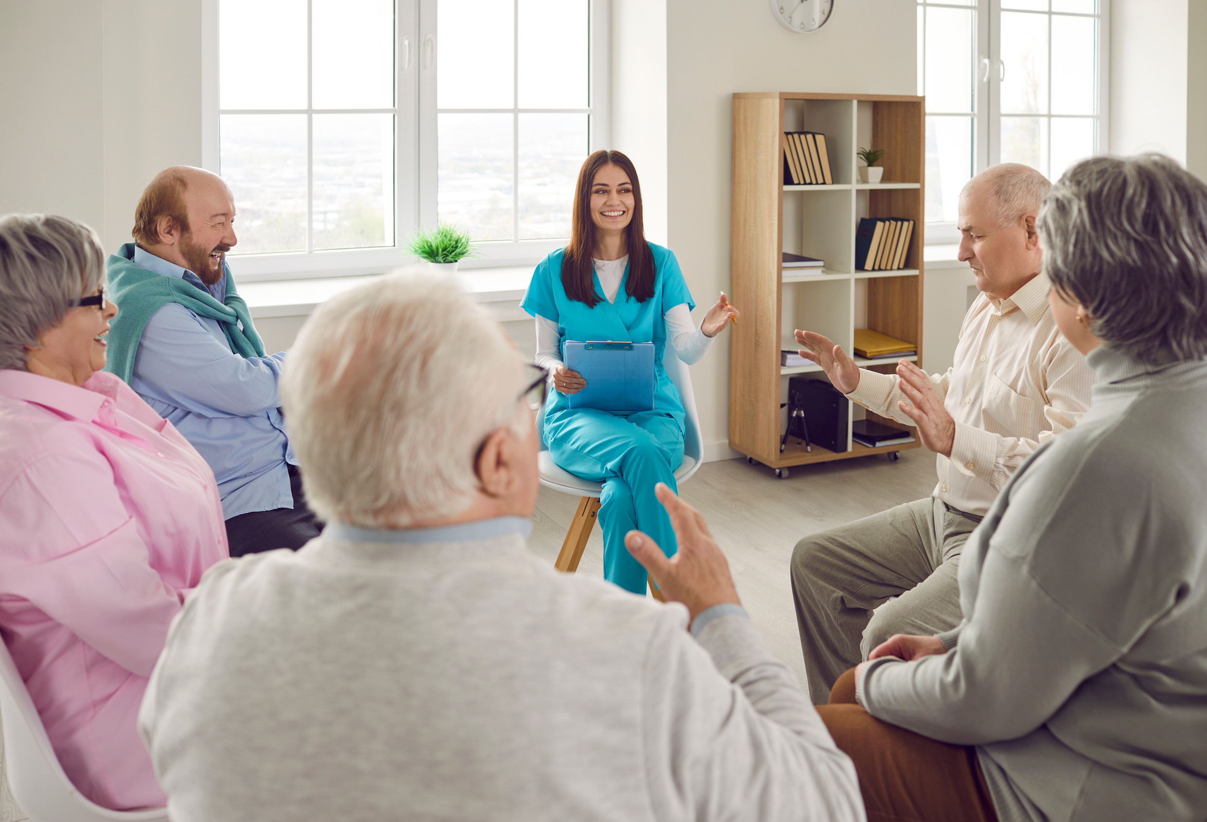 Young nurse and senior people in retirement home talking and having fun together