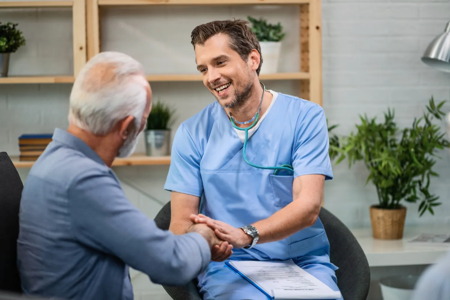 Happy general practitioner talking to senior man while shaking hands with him during a home visit Happy general practitioner talking to senior man while shaking hands with him during a home visit